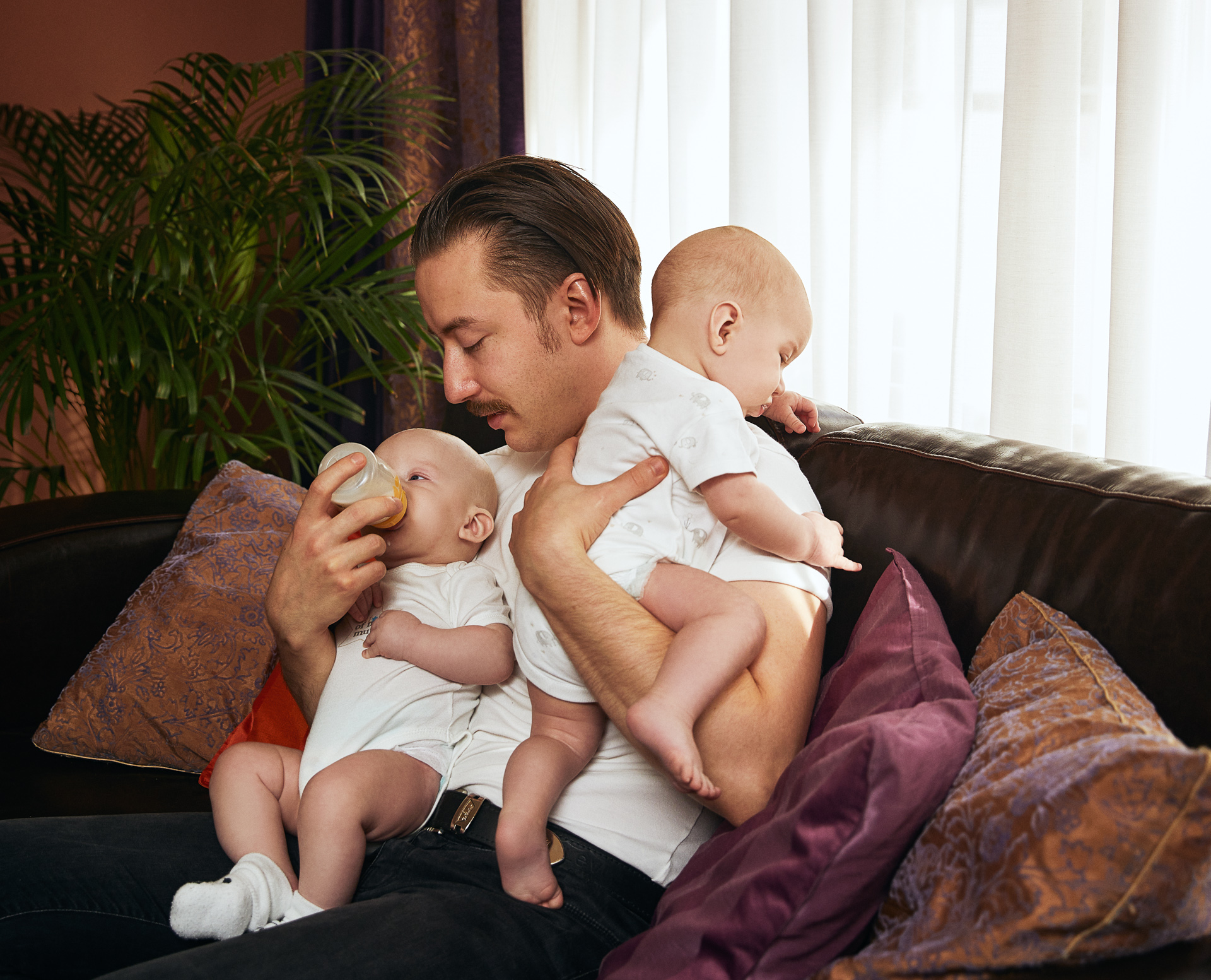 Vyras maitinantis kūdikius dvinukus ant rankų