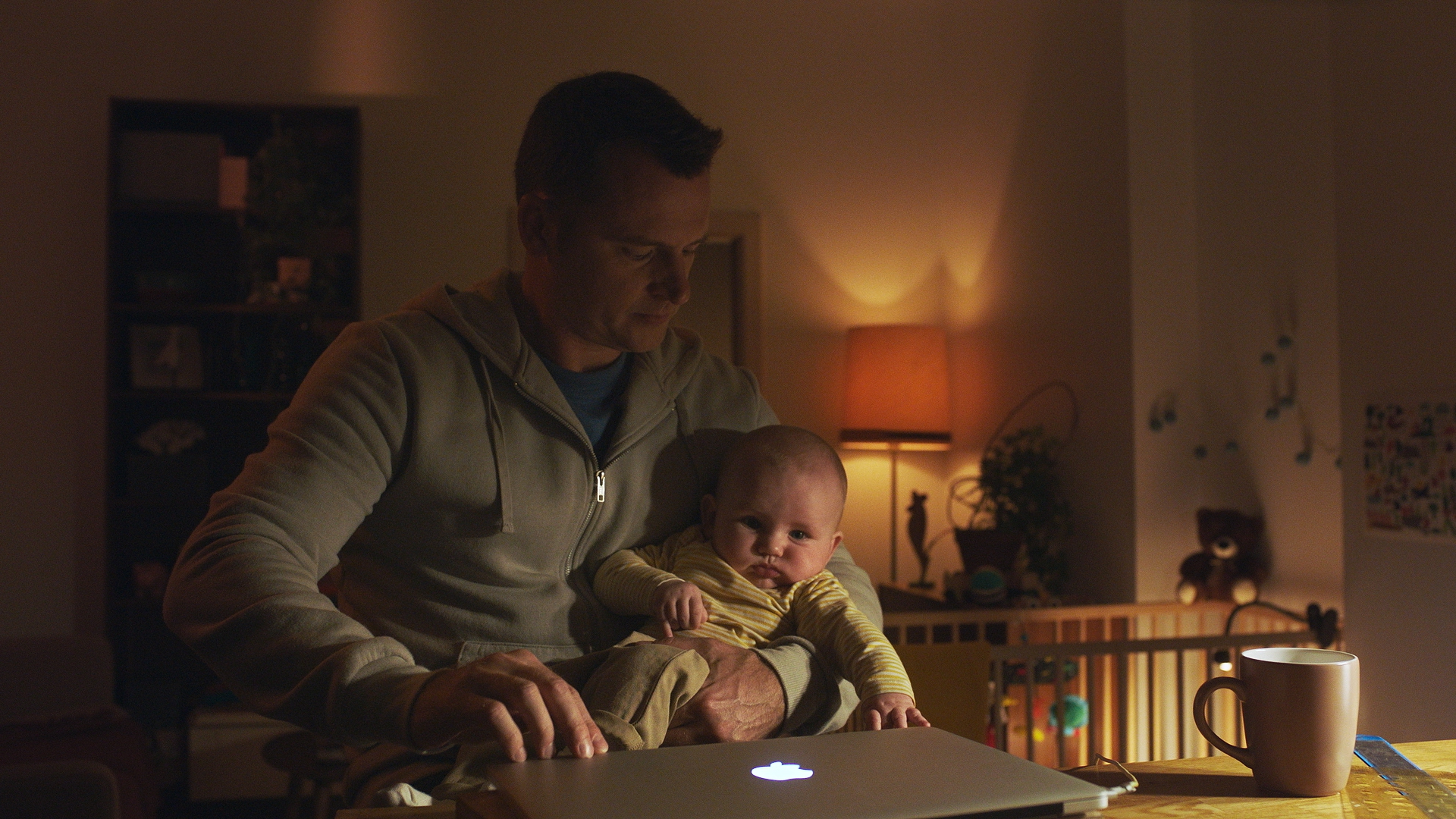 Tėtis su kūdikiu ant ranku prie kompiuterio