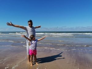 Tėtis su dukra iškeltomis rankomis į šoną prie jūros