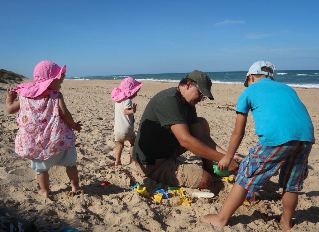Tėtis su trim vaikais stato smėlio pilį papludimyje