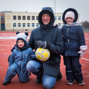 Tėtis su dviem vaikais futbolo lauke, pozuoja su kamuoliu