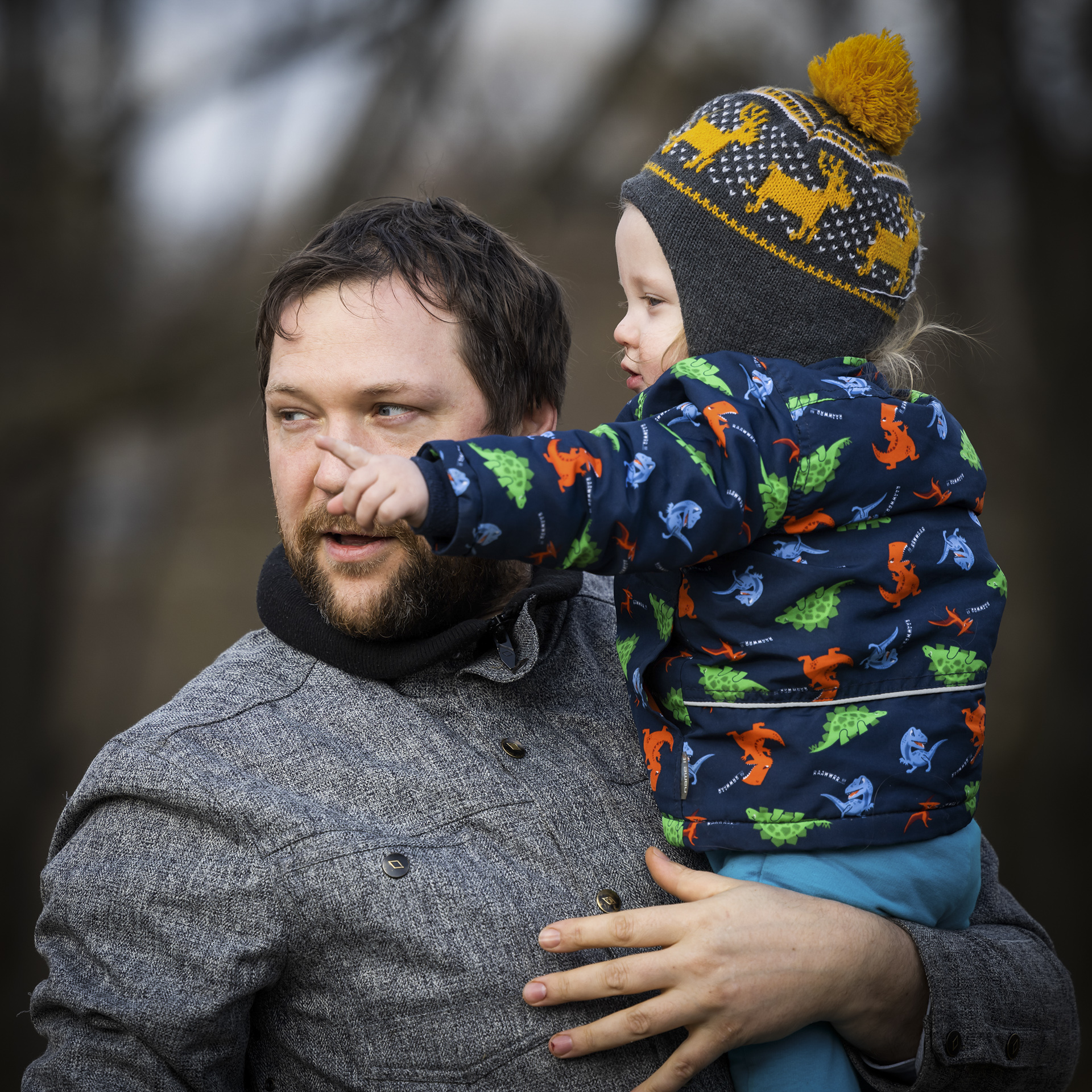 Tėtis ant rankų laiko vienerių metų sūnų, kuris kažką pirščiuku rodo į tolį