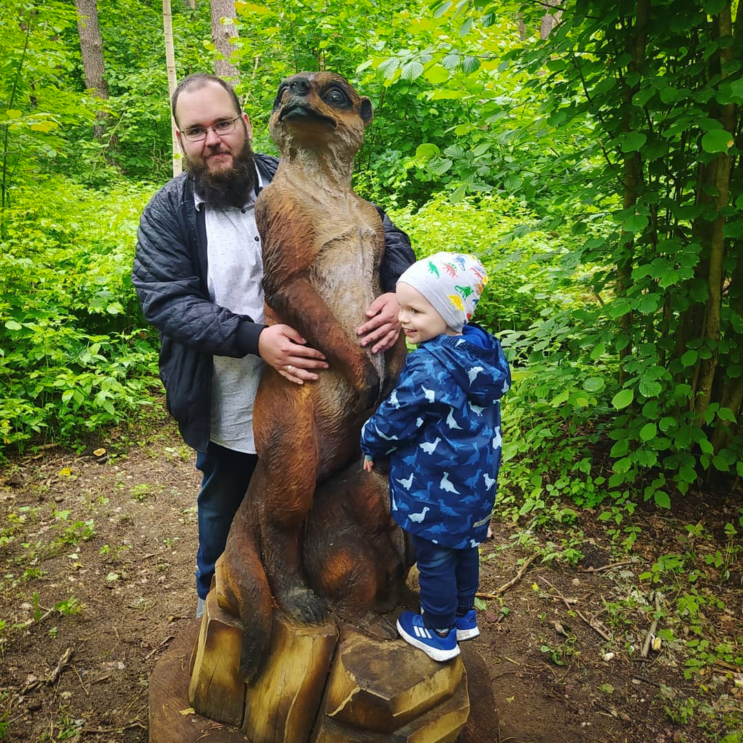 Tėtis su trimečiu sūnumi prie medinės skulptūros miške