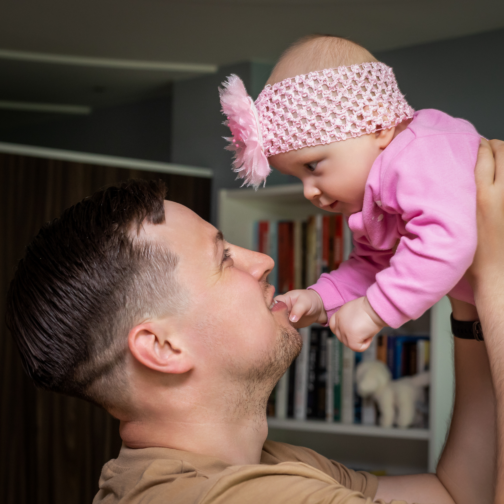 Tėtis virš galvos iškėlęs 6 mėnesių dukrytę, žiūri vienas kitam į akis