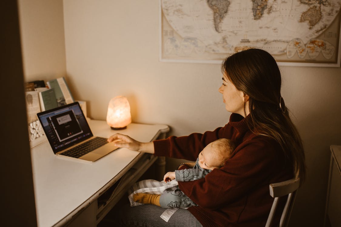Mama laiko kūdikį ant rankų ir dirba kompiuteriu