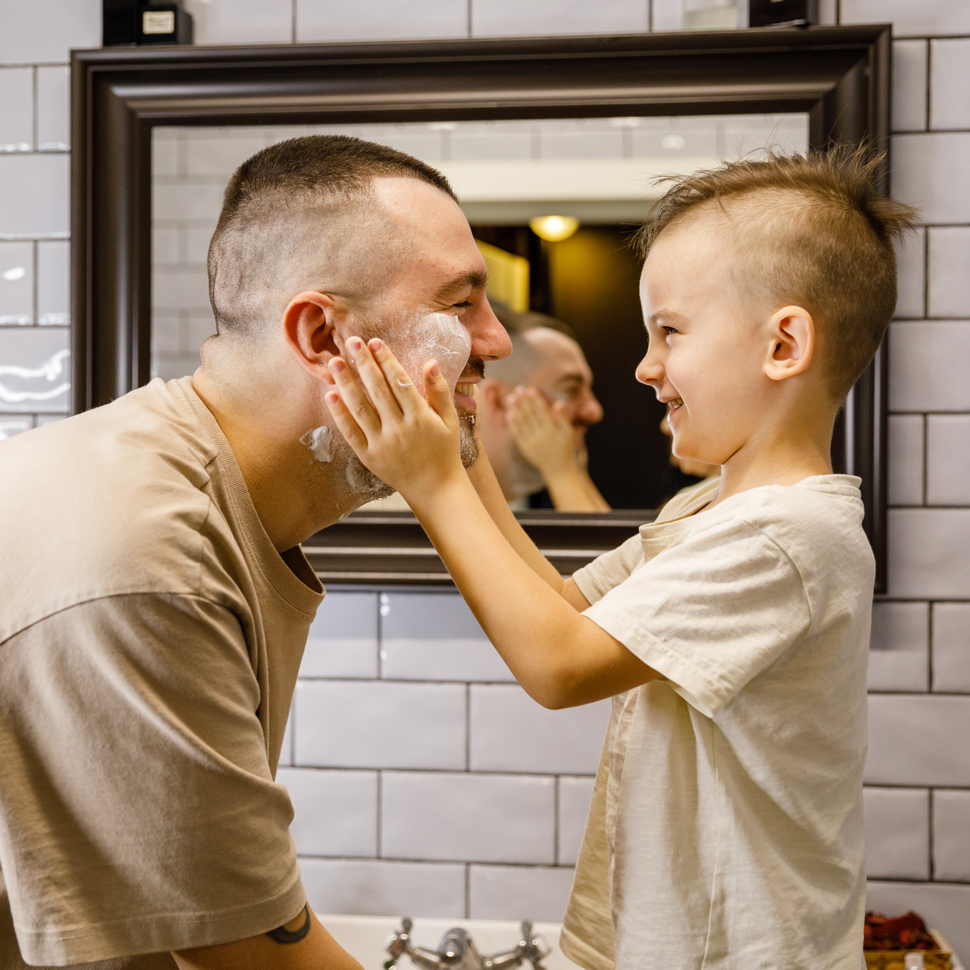 Tėtis su penkiamečiu vonioje, sūnus tepa tėčio veidą skutimosi putomis